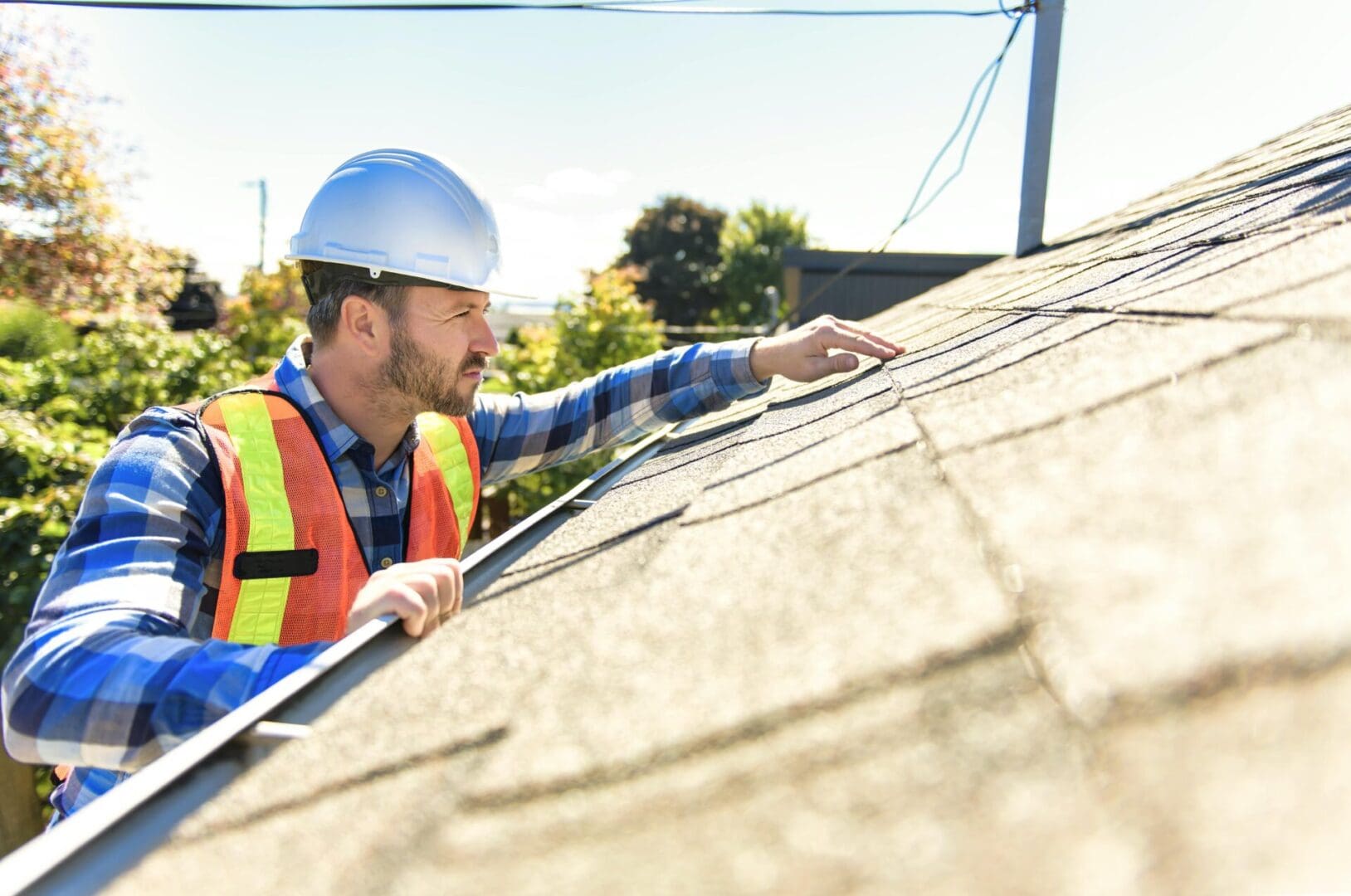 Construction worker inspecting roof shingles on a sunny day.