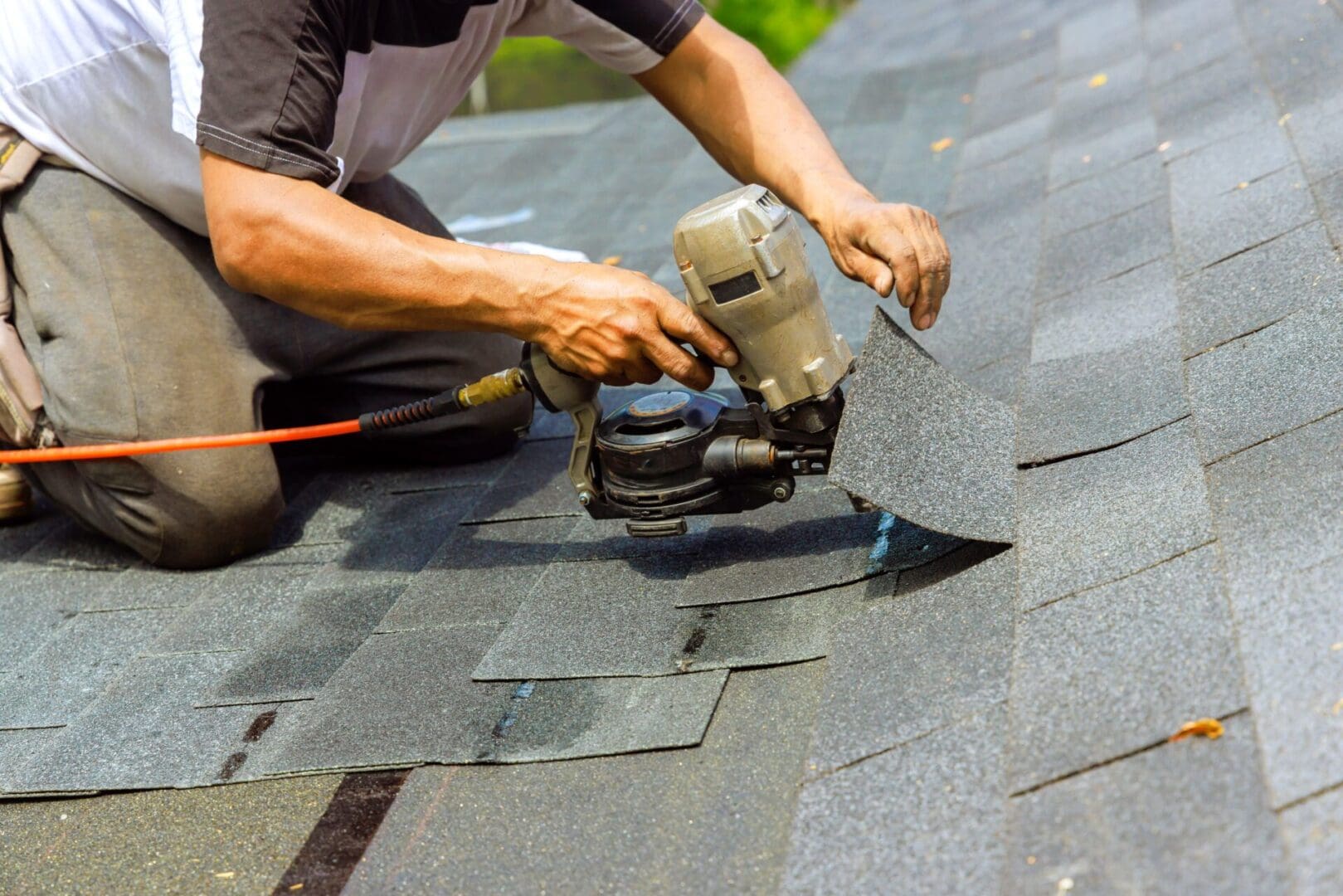 Worker installing asphalt shingles on a roof with a nail gun.
