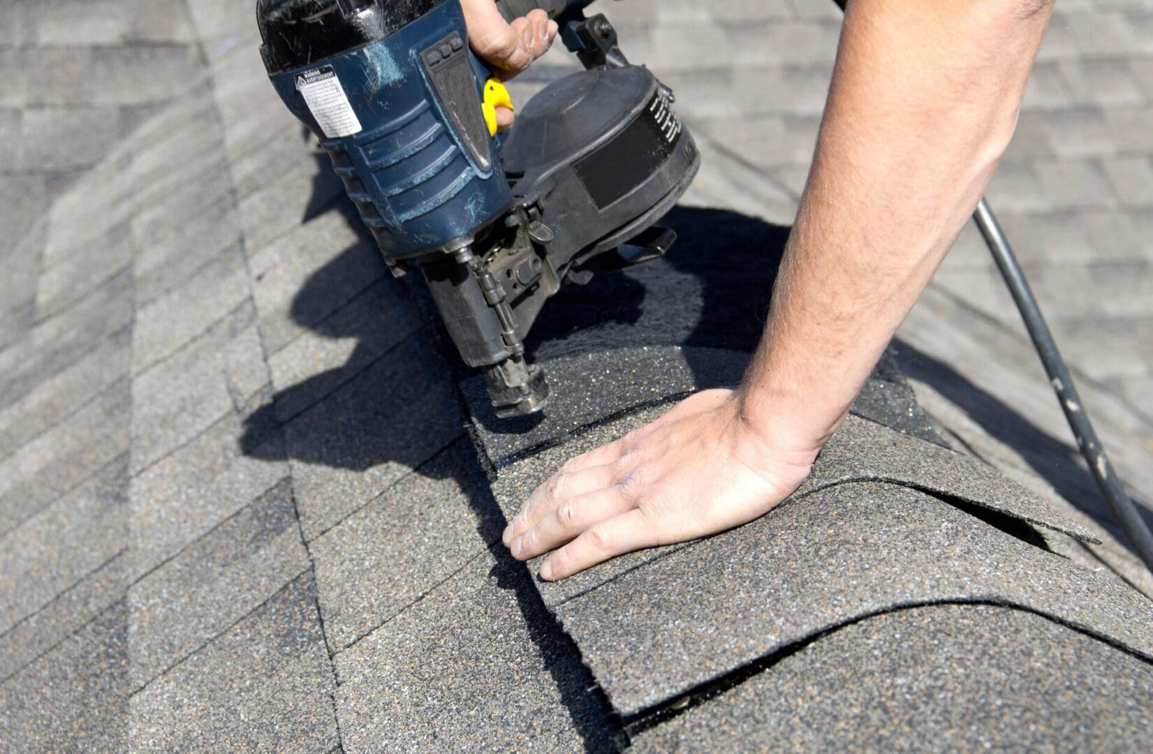 A worker uses a nail gun to secure roof shingles.