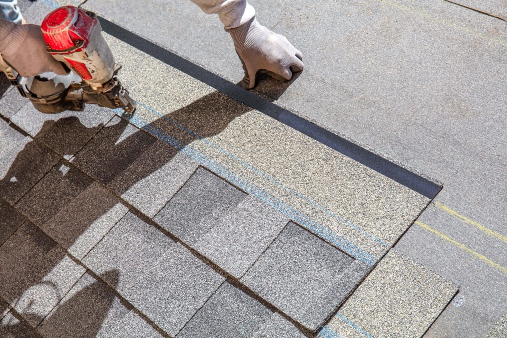 Hand installing asphalt shingles on a roof under bright sunlight.