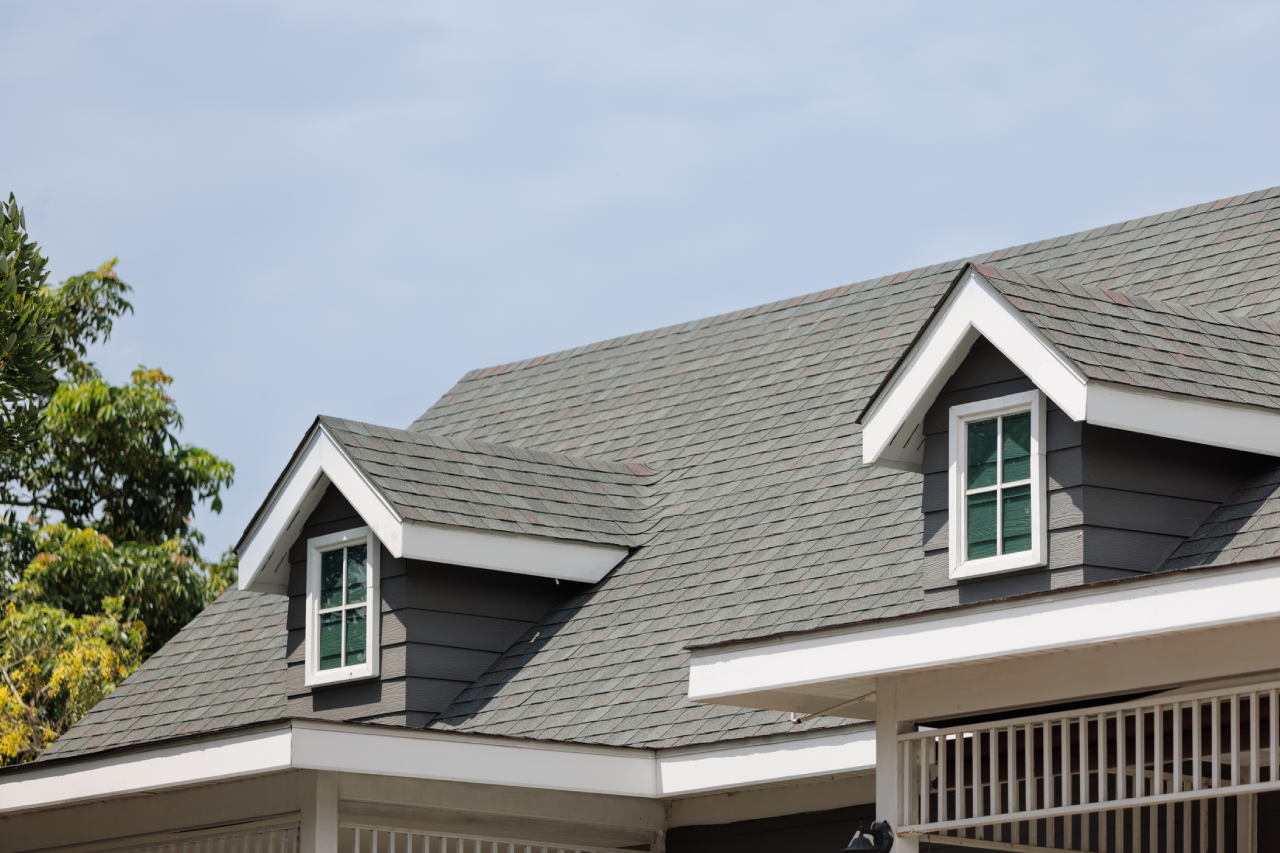 A house rooftop with two dormer windows and gray shingles.